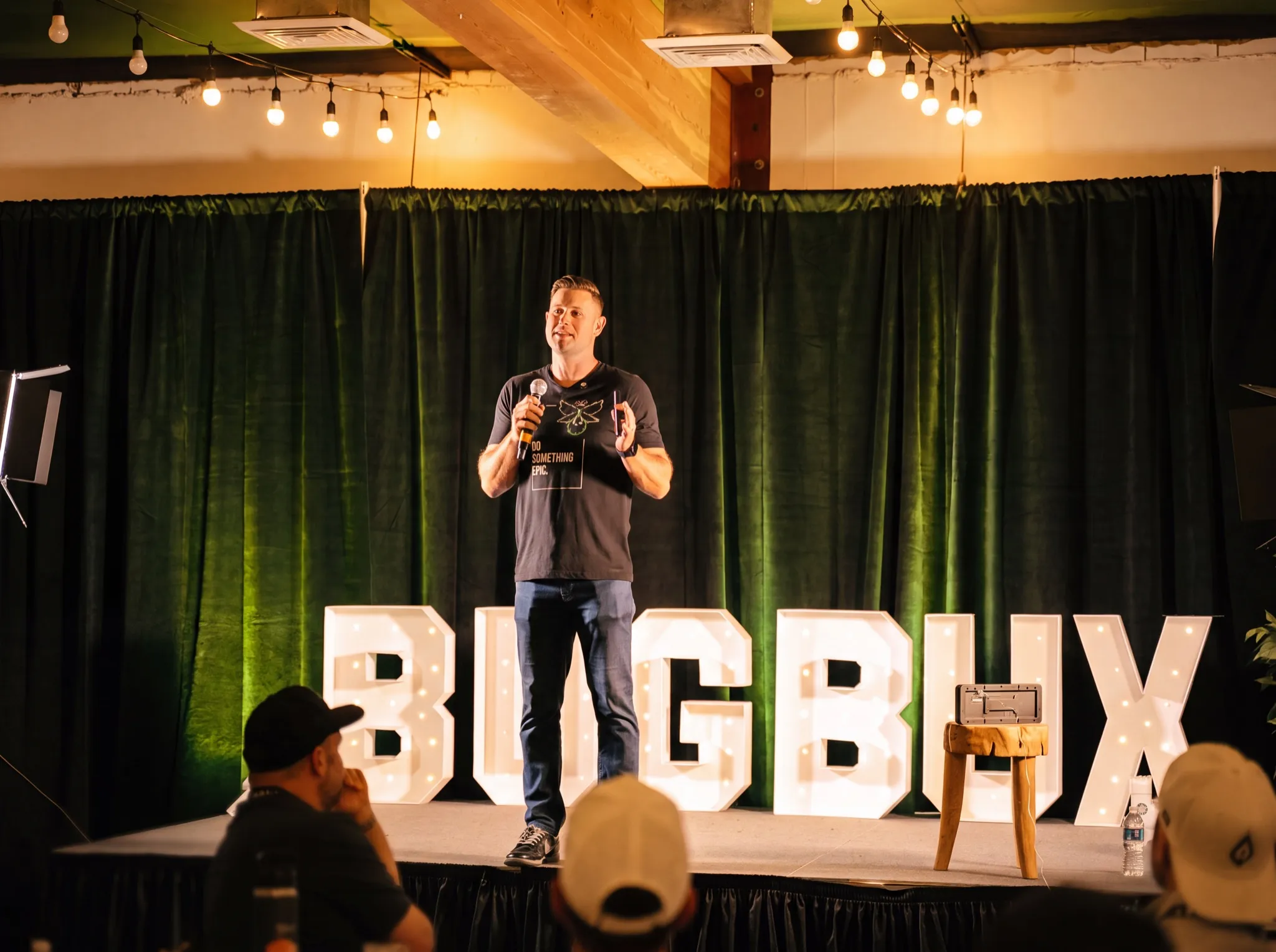 A speaker on stage in front of the lit Bug Bux sign at Bug Bux Con